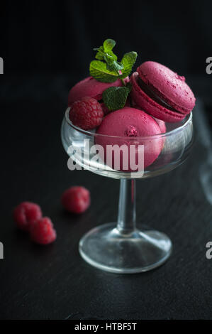 Amaretti rosa con lamponi in coppa su sfondo nero Foto Stock