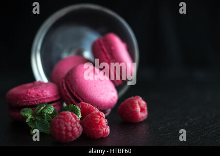 Amaretti rosa con lamponi in coppa su sfondo nero Foto Stock