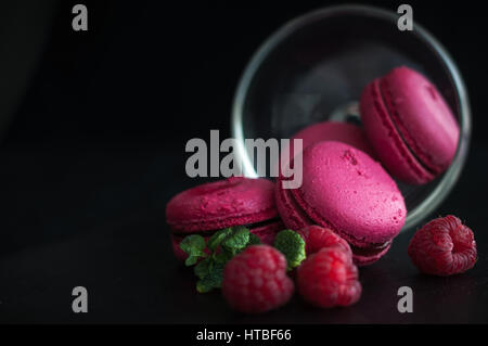 Amaretti rosa con lamponi in coppa su sfondo nero Foto Stock