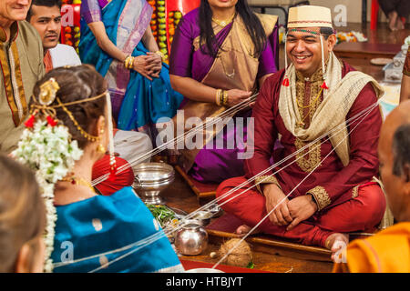 Il govern sorridente durante una portrion del suo Hindu / Indian nozze dove la sposa e lo sposo sono legati insieme e avvolto con la stringa che viene passata Foto Stock