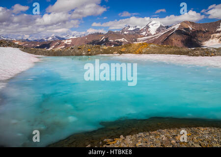 Una piscina di acqua giace su una patch di neve alta su una cresta nell'Alaska Range d'estate. La montagna sullo sfondo è bianco Princess Foto Stock