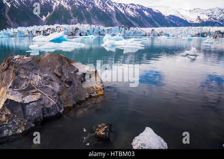 Un grosso masso si siede in una laguna contenente diversi iceberg partorito dalla faccia di Orso ghiacciaio (in background) nel Parco nazionale di Kenai Fjords Foto Stock