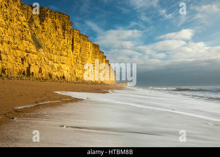 Onde che si infrangono sulla spiaggia al di sotto di East Cliff, West Bay, Jurassic Coast, Dorset, England, Regno Unito Foto Stock