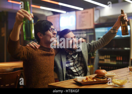 Uomini estatico con birra celebrando la vittoria della squadra di calcio Foto Stock