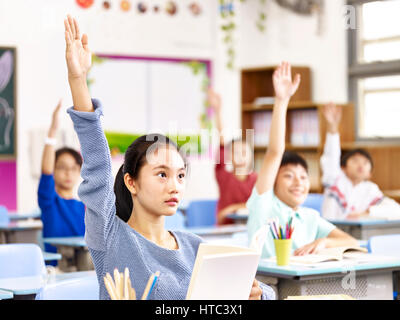 Asian scuola elementare ragazzi alzando le mani per rispondere alle domande durante le lezioni in classe. Foto Stock