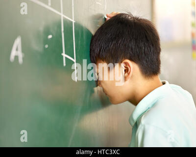 Dolorosa elementare asiatici schoolboy sbattendo la testa su lavagna pur risolvendo il problema di geometria. Foto Stock