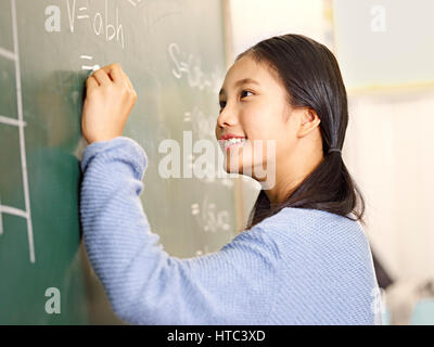 Fiducioso asiatici scuola elementare studente che scrive la risposta a un problema di geometria sulla lavagna. Foto Stock