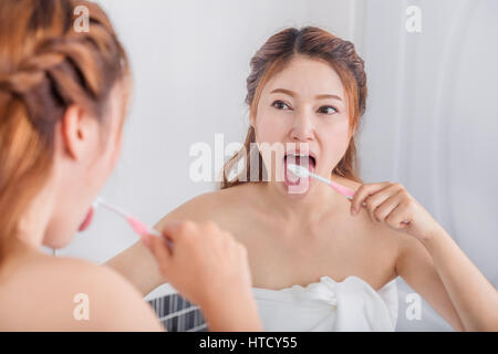 Donna linguetta di pulizia utilizzando uno spazzolino da denti con specchio del bagno Foto Stock