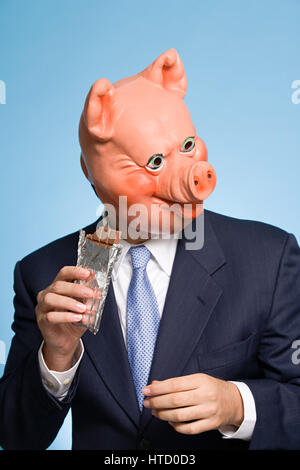 Uomo in una maschera di maiale mangiare il cioccolato Foto Stock