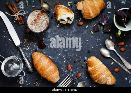 Caffè, croissant, cioccolata, spezie, dadi e posate vintage. Piano di composizione dei laici di dolce colazione il cibo sulla pietra scura con sfondo spazio copia Foto Stock