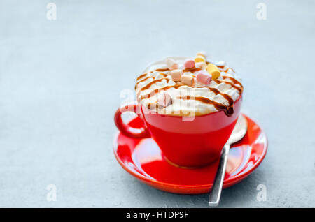 Red cup con latte con crema di caramello e pezzi di marshmallow colorati su un bel bianco superficie di legno. Foto Stock