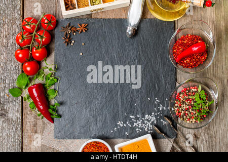 Sfondo di cibo, con spazio per il testo, erbe aromatiche, spezie, olio d'oliva, sale e verdure. Ardesia e uno sfondo di legno. Vista superiore Foto Stock
