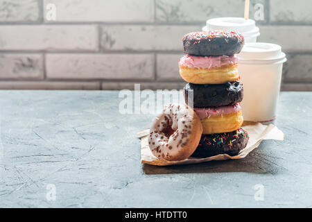 Pila di ciambelle assortite su un foglio di carta con caffè su sfondo grigio Foto Stock