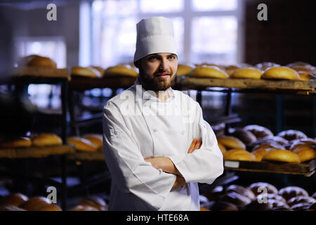 Giovane uomo bello baker in bianco uniforme e il tappo sul forno di sfondo Foto Stock