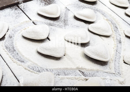 Impasto crudo a forma di cuore (pierogi, ravioli, gnocchi), spargimento farina steso su un legno scuro dello sfondo. Foto Stock