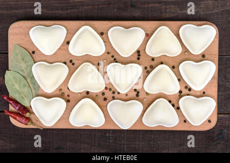 Pasta cruda in forma di cuore (gnocchi di patate, ravioli, pelmeni), su di un tagliere. Vista superiore Foto Stock