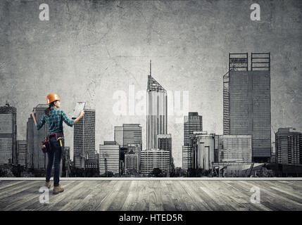 Vista posteriore di ingegnere di donna con la cartella e schizzi di progetto di costruzione sulla parete Foto Stock