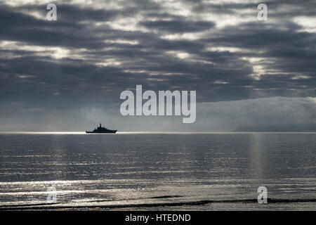 Metal detectorist sulla spiaggia di Paignton caccia al tesoro,un mezzo navale si siede in Torbay con Berry Head in background  Foto Stock