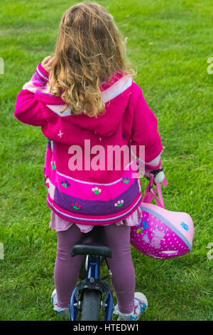 Vista posteriore del giovane ragazza in piedi a cavallo bike azienda casco ciclo a Poole, Dorset nel mese di settembre Foto Stock