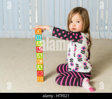 Giovani femmine toddler la costruzione di una torre di blocchi di legno a casa Obamacare ortografia Foto Stock
