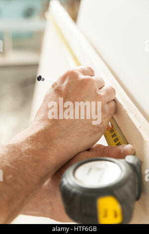 Le mani di un falegname misurando con un nastro e wiriting giù sul pannello di legno con una matita; nozione di falegname artigiano nella sua bottega Foto Stock