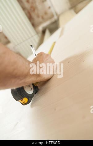 Le mani di un falegname misurando con un nastro e wiriting giù sul pannello di legno con una matita; nozione di falegname artigiano nella sua bottega Foto Stock