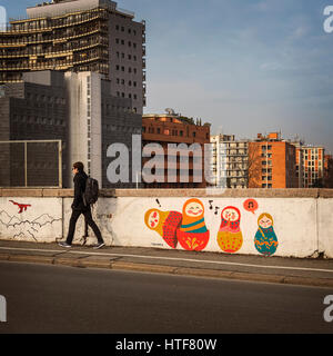 BOLOGNA, Italia - 08 febbraio, 2017. Uomo che cammina attraverso la via via Stalingrado, passando la street art con il moderno parti dello skyline della città in backgro Foto Stock