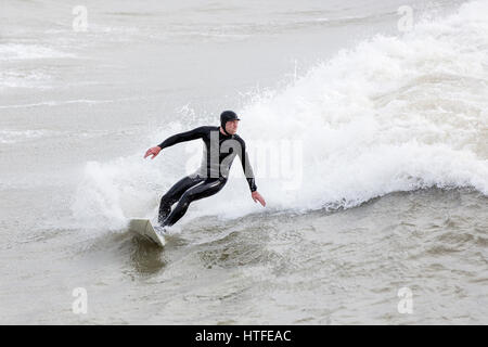 Un surfista sfrutta il mare in tempesta a Bournemouth Dorset, Inghilterra e cavalca una grande onda voce a riva Foto Stock