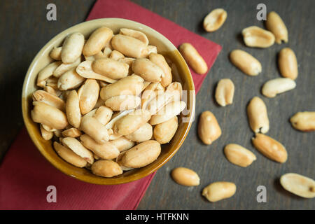 Sbucciate tostate arachidi salate nel recipiente rustico su sfondo di legno (focus su peanut nel recipiente) Foto Stock