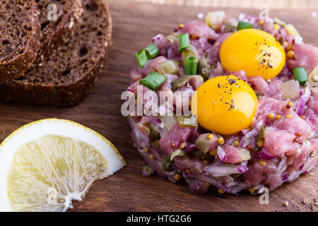 Tartare di manzo sagomato in stampo ad anello, guarnita con due uova di quaglia tuorli e servita con pane di segale sul tagliere di legno Foto Stock