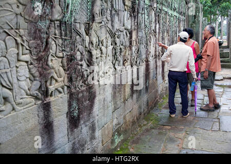 Scena di battaglia bassorilievi e turisti in Angkor Thom tempio. I templi di Angkor, Cambogia, Asia Foto Stock