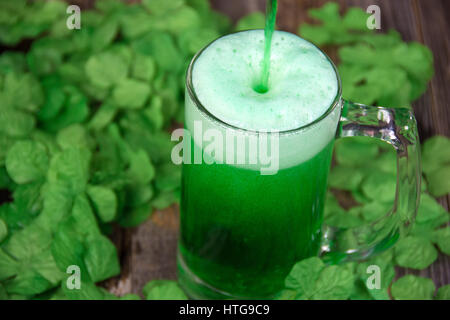 Birra verde in tazza con trifogli irlandesi su legno Foto Stock