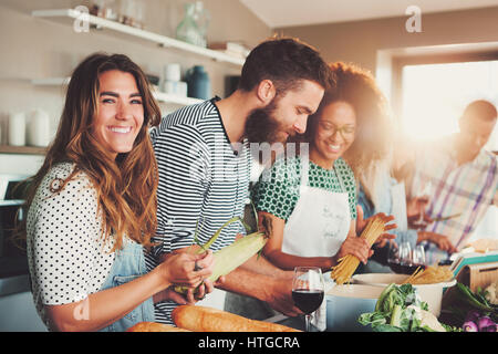 Multirazziale amici divertenti cuocere qualche gustoso cibo in cucina mentre si beve vino. Vista laterale. Foto Stock