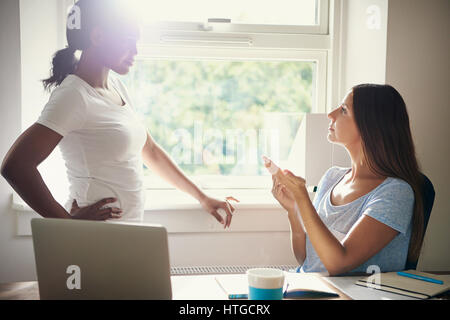 Due giovani imprenditrice avente una discussione in ufficio di fronte a una finestra luminosa con sun flare in un lavoro di squadra, partenariato e entrepreneu femmina Foto Stock