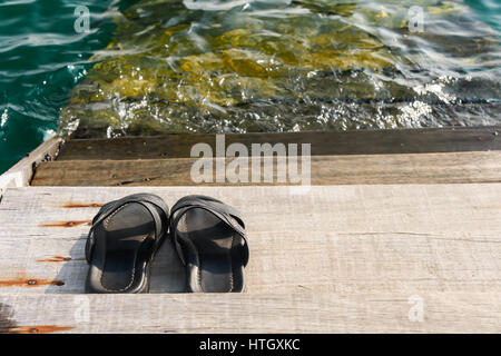 Coppia di black mens sandals flip flop su un listone a waterfront Foto Stock