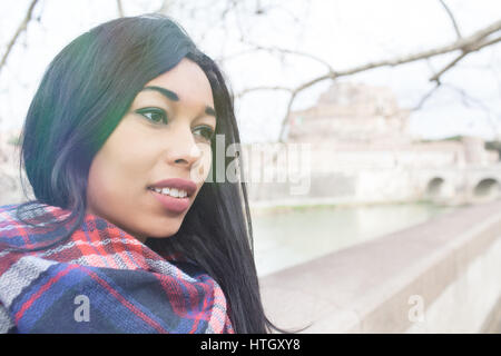 Giovane bella gara di misto donna con espressione malinconica, guardando oltre a Roma, in Italia con Sant Angelo il castello e il fiume Tevere in background di un Foto Stock