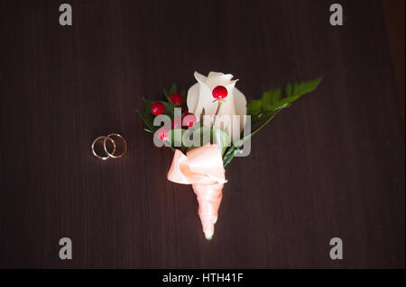 Accessori di nozze su sfondo scuro lo sposo prima della cerimonia: boutonniere, anelli oro. govern boutonniere di fiori freschi: Rose bianche, verde Foto Stock