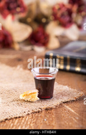 Tenendo la comunione. Bicchiere di vetro con il vino rosso, il pane e la Santa Bibbia sul tavolo di legno di close-up. La messa a fuoco su vetro Foto Stock