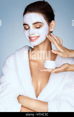 Ragazza sorridente con idratante maschera per il viso e le mani del parrucchiere. Foto della bella ragazza elegante riceve i trattamenti della spa. Bellezza & pelle auto Foto Stock