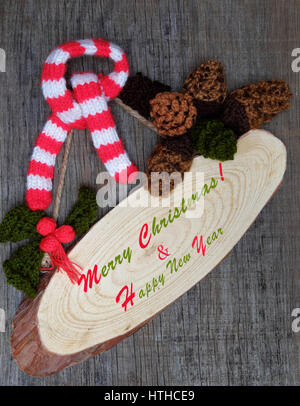 Bella artigianale di ornamento per le vacanze invernali, gruppo del tessuto lavorato a maglia a Pigna, holly leaf, bacche lavorato a maglia di filati, messaggio Buon Natale su tag, nice Xmas ba Foto Stock