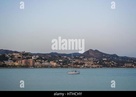 Un solitario barca da pesca in mare Meditarrain con la città e le montagne sullo sfondo la sera vicino a Malaga, Andalusia, Spagna. Foto Stock