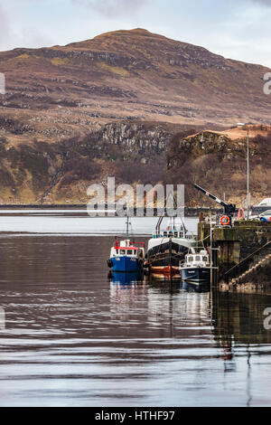 Ben Tianavaig sul Loch Portree, sull'Isola di Skye in Scozia, contro un cielo drammatico, dietro alla fine del molo del porto e le barche Foto Stock