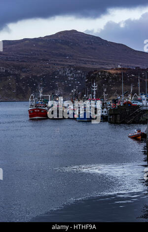 Ben Tianavaig sul Loch Portree, sull'Isola di Skye in Scozia, contro un cielo drammatico, dietro alla fine del molo del porto e le barche Foto Stock