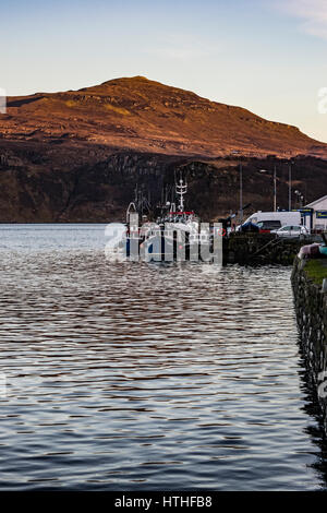 Ben Tianavaig sul Loch Portree, sull'Isola di Skye in Scozia, contro un chiaro cielo di sera, dietro alla fine del molo del porto e le barche Foto Stock