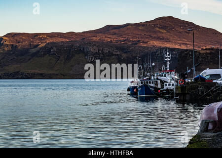 Ben Tianavaig sul Loch Portree, sull'Isola di Skye in Scozia, contro un chiaro cielo di sera, dietro alla fine del molo del porto e le barche Foto Stock