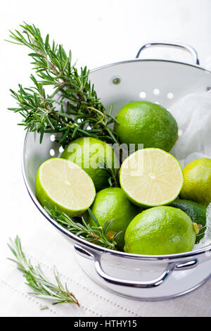 Limette fresche e rosmarino molle in smalto bianco scolapasta. Foto Stock