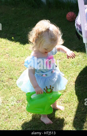 Bambini che giocano in giardino, vestiti con i loro costumi principessa, Cenerentola, dressup portando un annaffiatoio conformata come una rana che indossa una corona Foto Stock