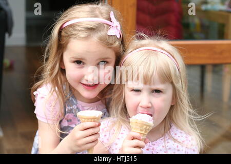 Ragazze bionde bambini mangiare leccare leccare coni gelato su una giornata d'estate bambini dolce godendo di coni gelato felice concetto, i gemelli, fratelli concept Foto Stock