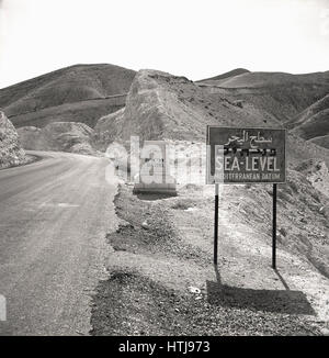 Degli anni Cinquanta, foto storiche che mostra due livello del mare segni accanto a una strada di montagna, Giordania. Foto Stock