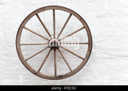 Vecchio carrello di legno ruota sospesa sul bianco parete rurale Foto Stock